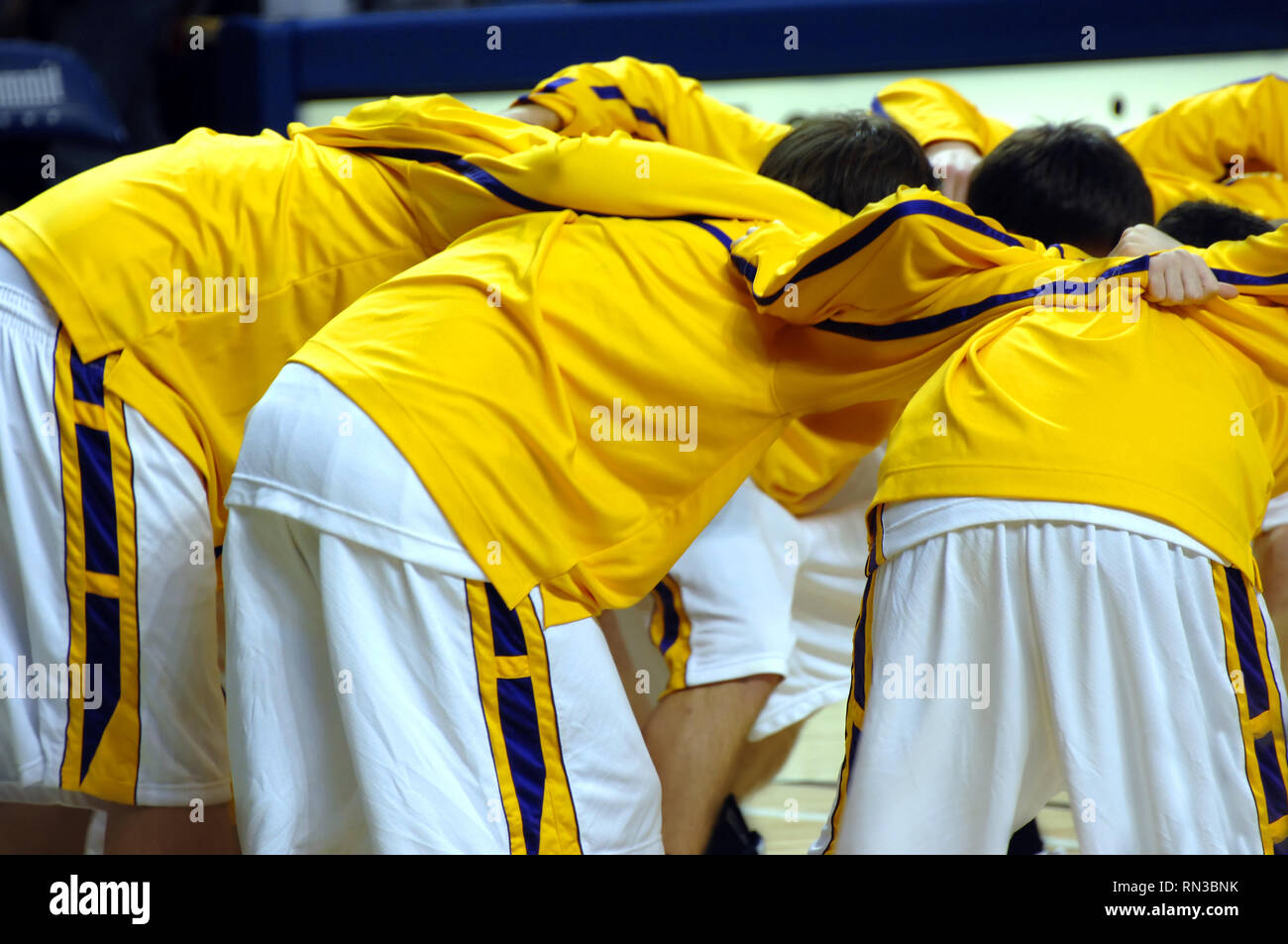 High School Varsity Basketball team Unordnungen zusammen vor dem Spiel starten. Uniformen sind Gelb, Violett und Weiß. Stockfoto