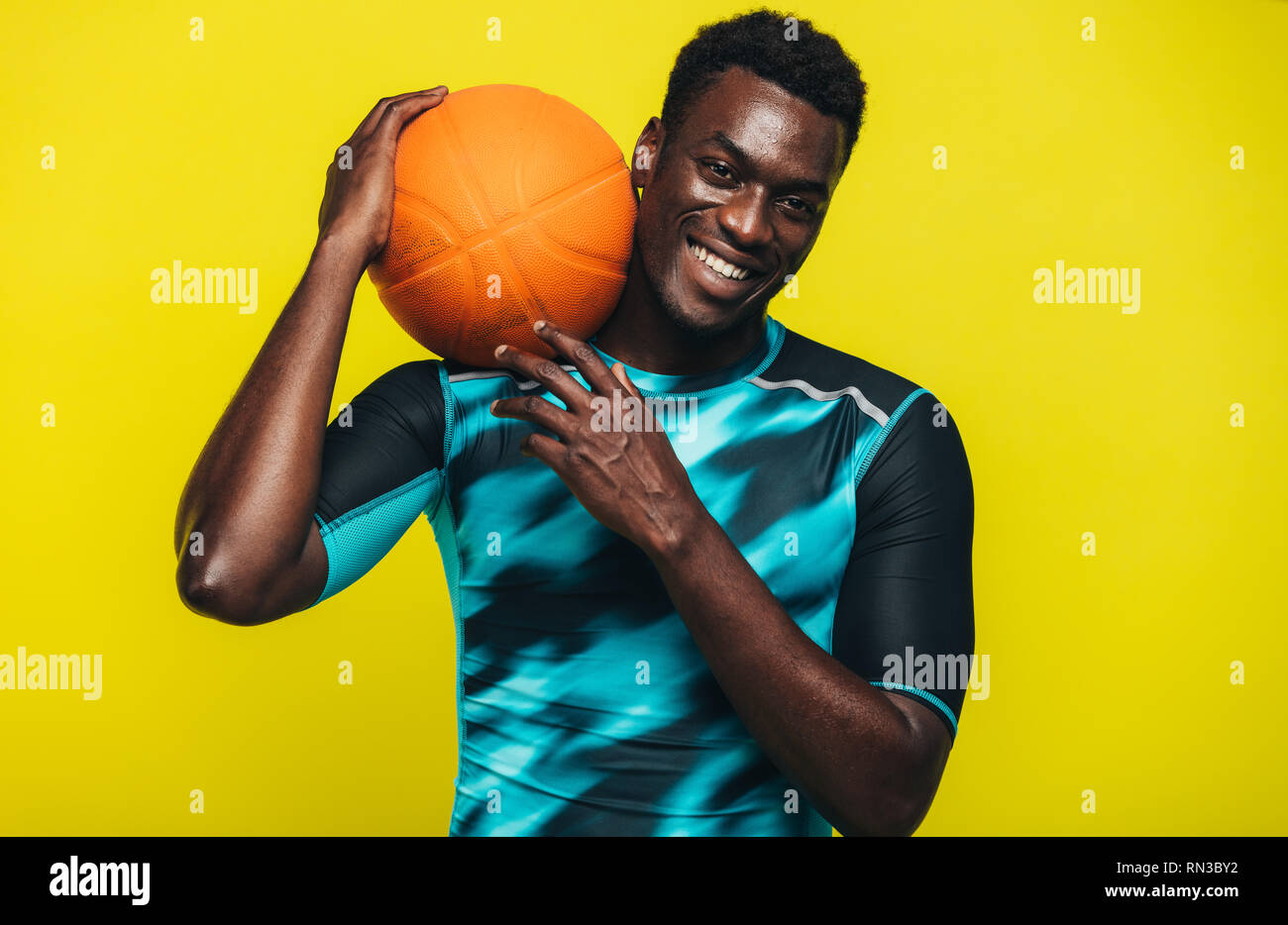 Lächelnd afrikanischen Mann mit Basketball an der Kamera schaut. Junge Basketball Spieler gegen gelben Hintergrund. Stockfoto