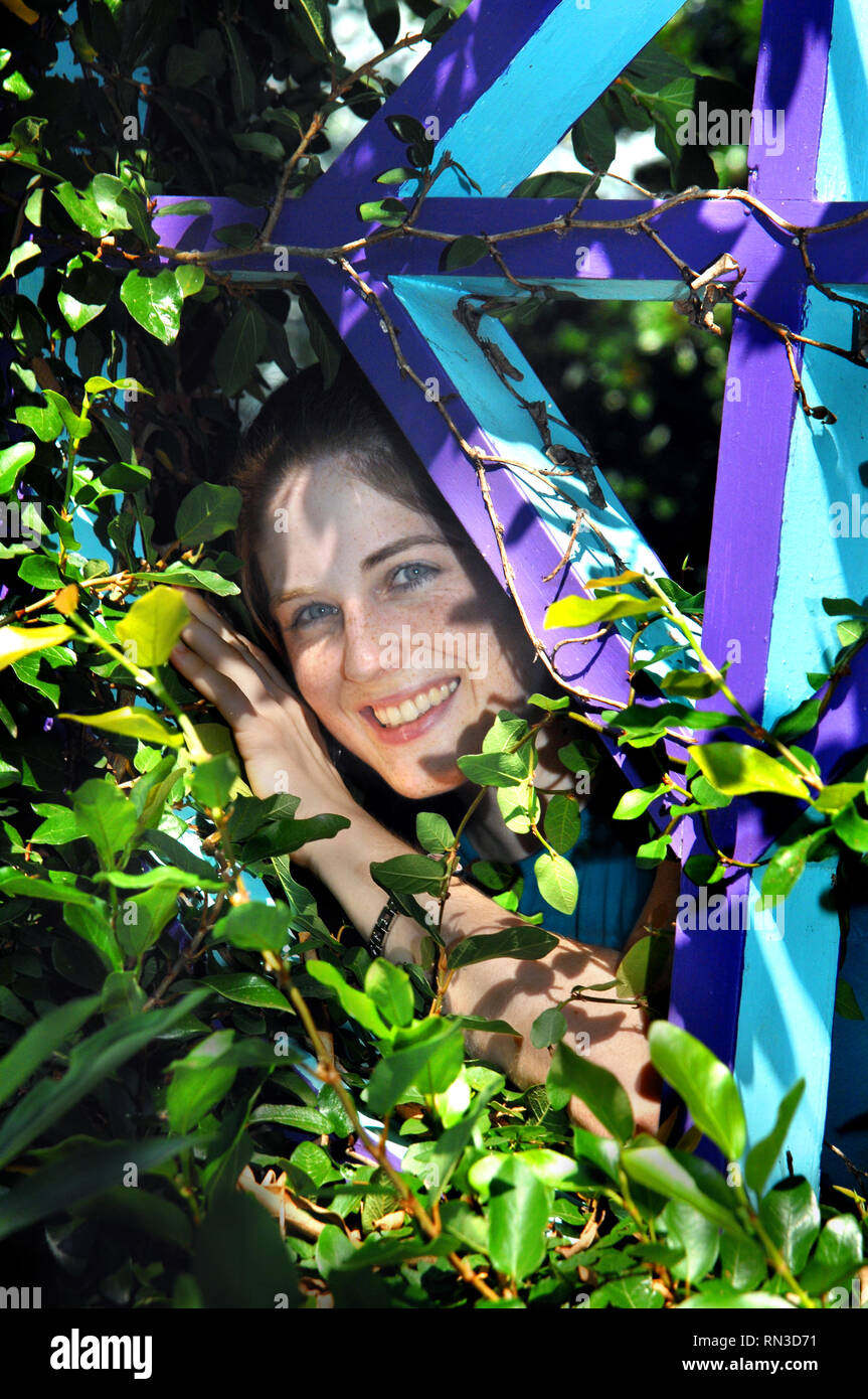 Junge Frau spielt peek-a-boo in einem Garten in Columbia, South Carolina. Sie strahlt mit Sommersprossen und Frische. Stockfoto