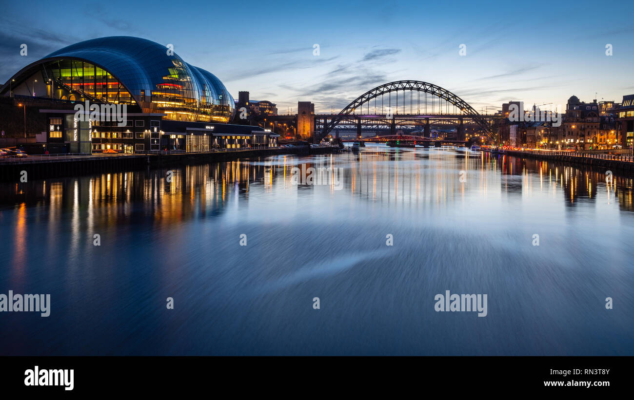 Gateshead, England, Großbritannien - Februar 6, 2019: Die Sage Gateshead Gebäude und ikonischen Tyne Bridge Leuchten in der Dämmerung auf dem Fluss Tyne. Stockfoto