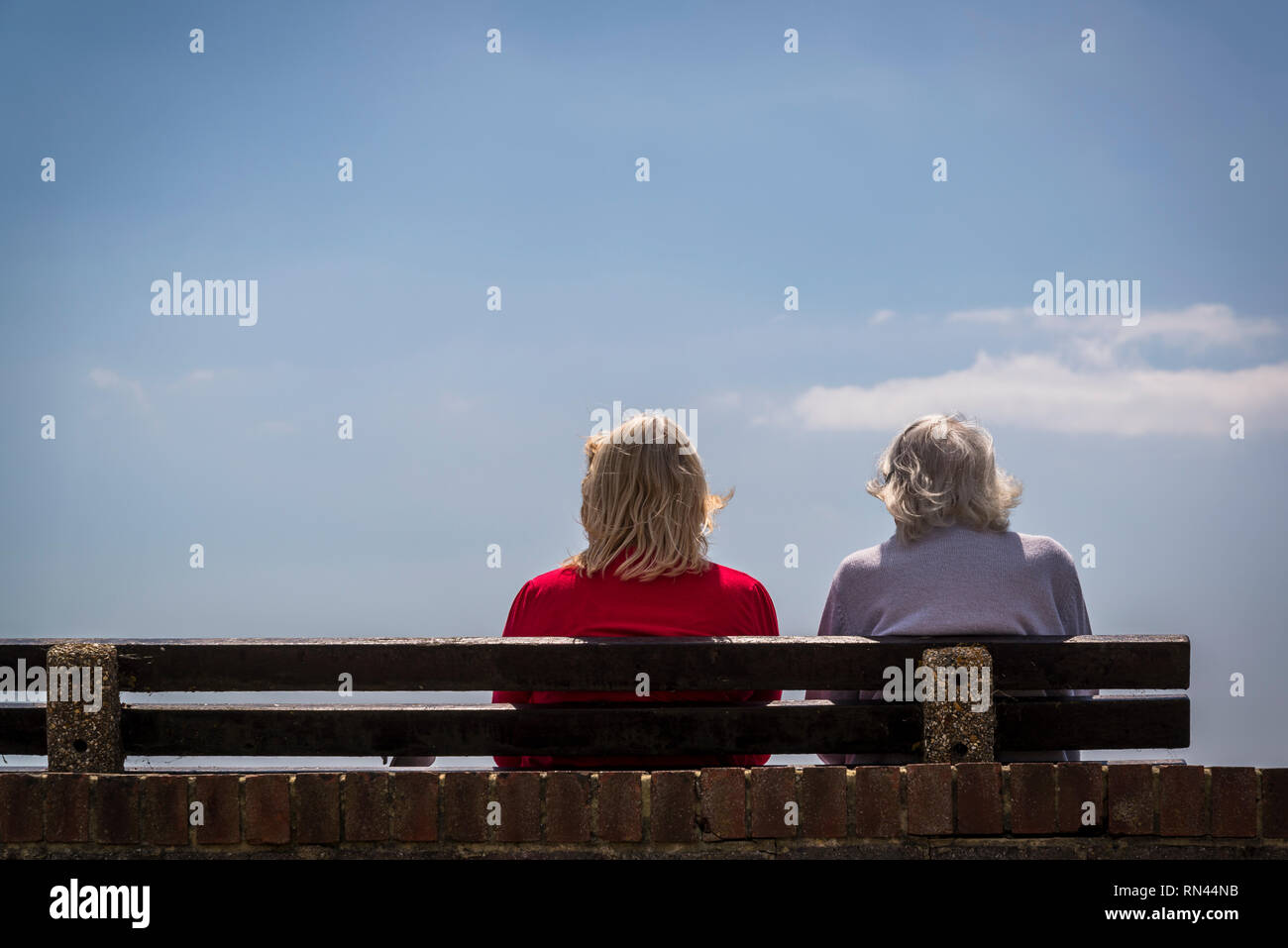 Zwei Frauen, ältere Mutter und Tochter im mittleren Alter auf einer Bank sitzen und auf das Meer, Littlehampton, West Sussex, England, Großbritannien Stockfoto