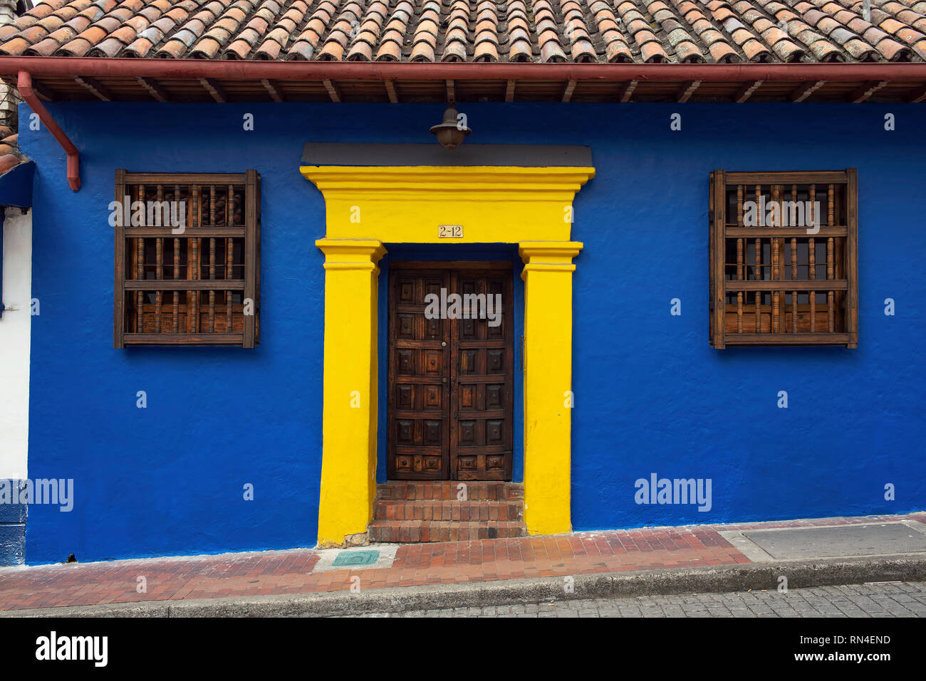 Elegante koloniale Fassade mit Holz geschnitzte Tür und Blau-gelbe Wand (komplementärer Farbkontrast) in La Candelaria. Bogota, Kolumbien. Sep 2018 Stockfoto