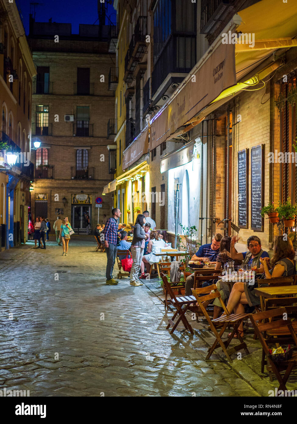 Menschen in Cafes sitzen am frühen Abend in einer Seitenstraße in Sevilla, Spanien. Stockfoto