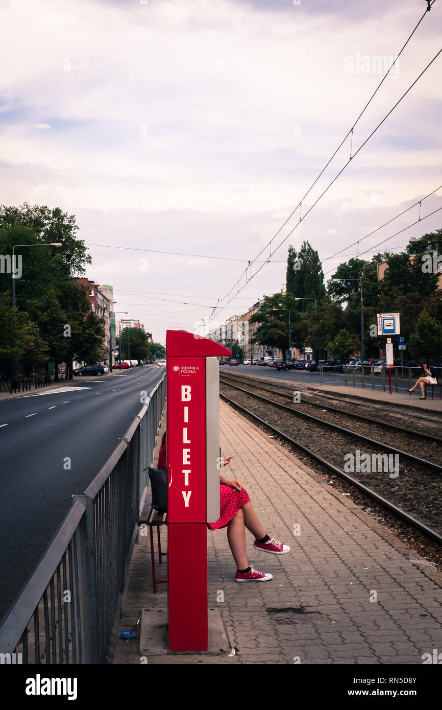 Frau in einem roten Kleid mit roten Schuhen sitzen auf einem Bahnsteig hinter einem roten Fahrkartenautomaten ausgeblendet Stockfoto