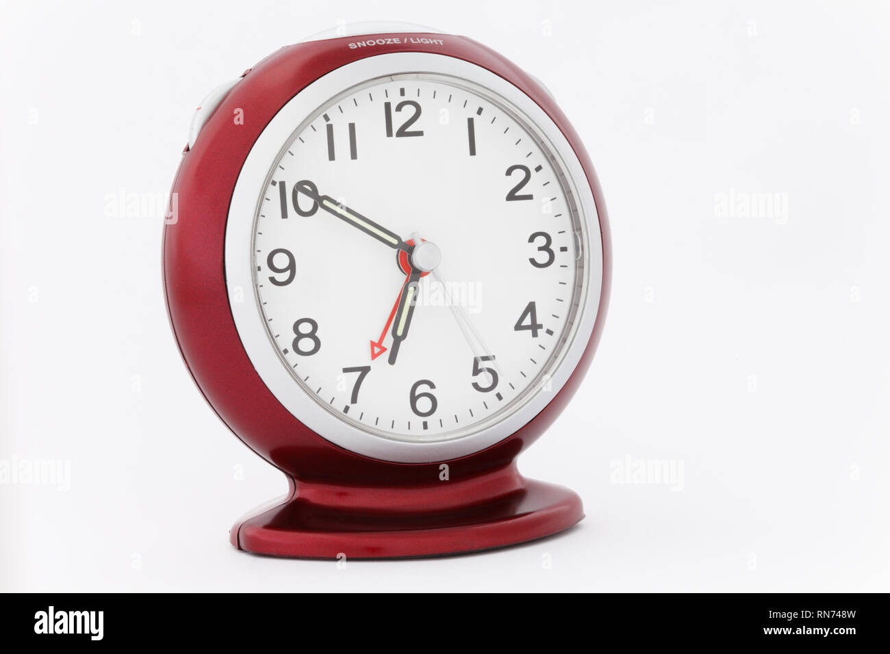 Roter analoger Wecker mit leuchtenden Zeigern, die die Zeit von zehn Minuten bis sieben kurz vor dem Weckton am Morgen anzeigen. Perfektes Timing-Konzept Stockfoto