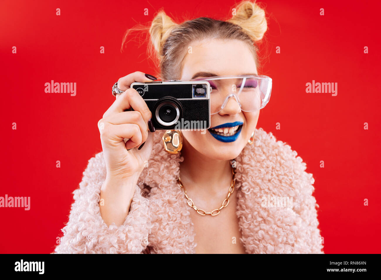 Frau mit blauen Lippen und rosa Schlafbrillen mit Kamera Stockfoto