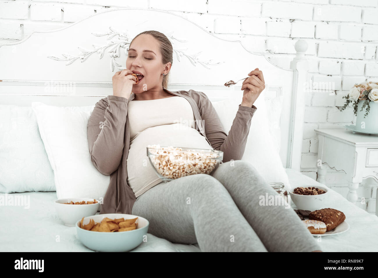 Langhaarige schwangere Frau im Bett sitzen und essen Stockfoto