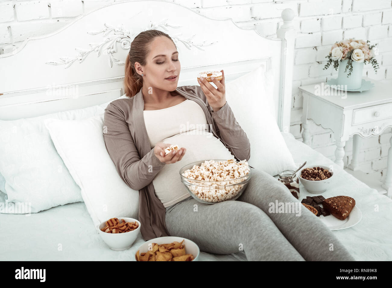 Dicke schwangere Frau in Pastelltönen Outfit im Bett lag und die Durchführung donut Stockfoto