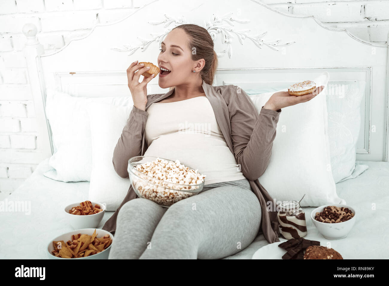 Fröhliche dicke Frau im Bett liegt und sich Füllen mit Junk Food Stockfoto
