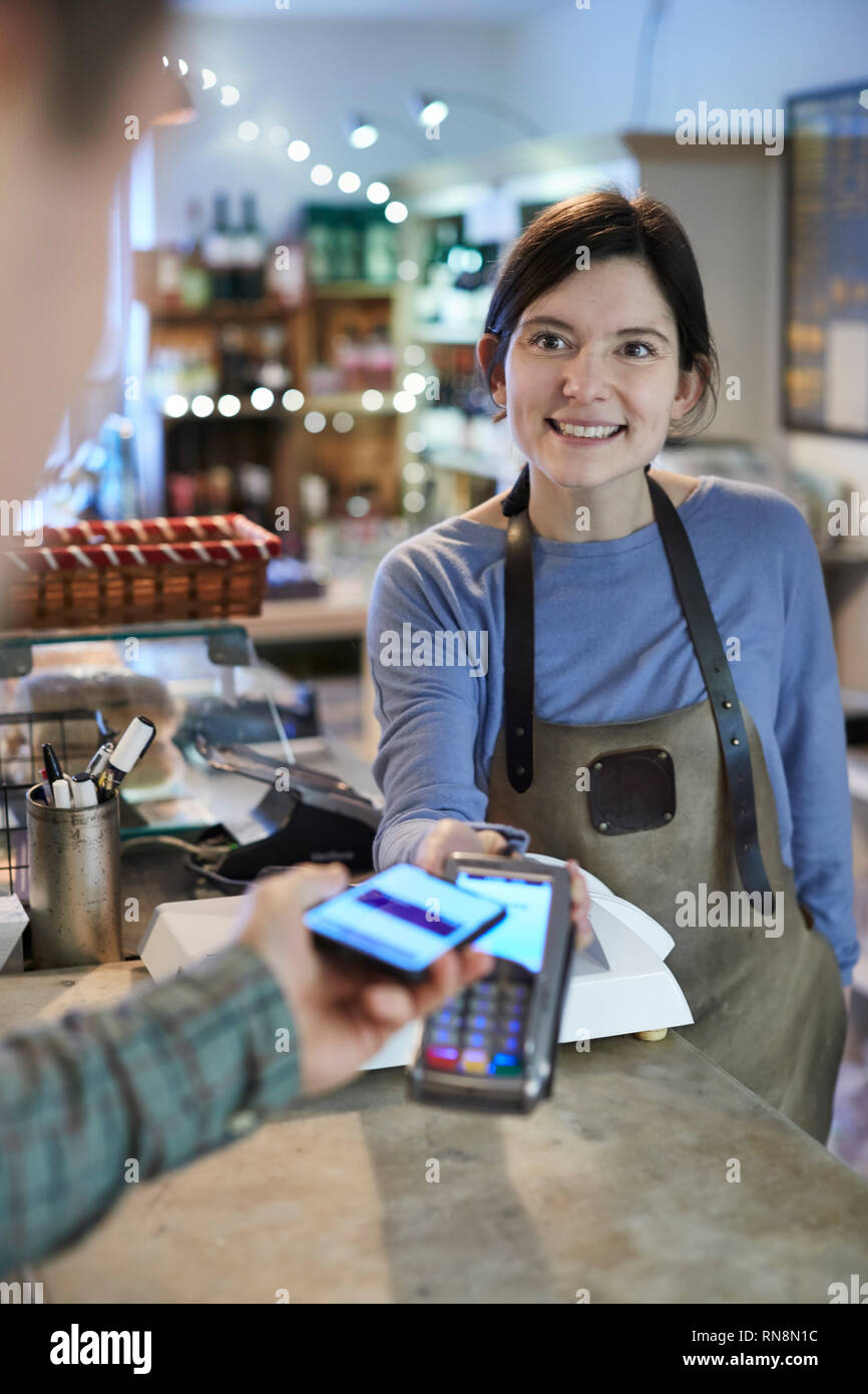 Männliche Kunden kontaktloses Bezahlen für das Einkaufen über Handy in Feinkost Stockfoto