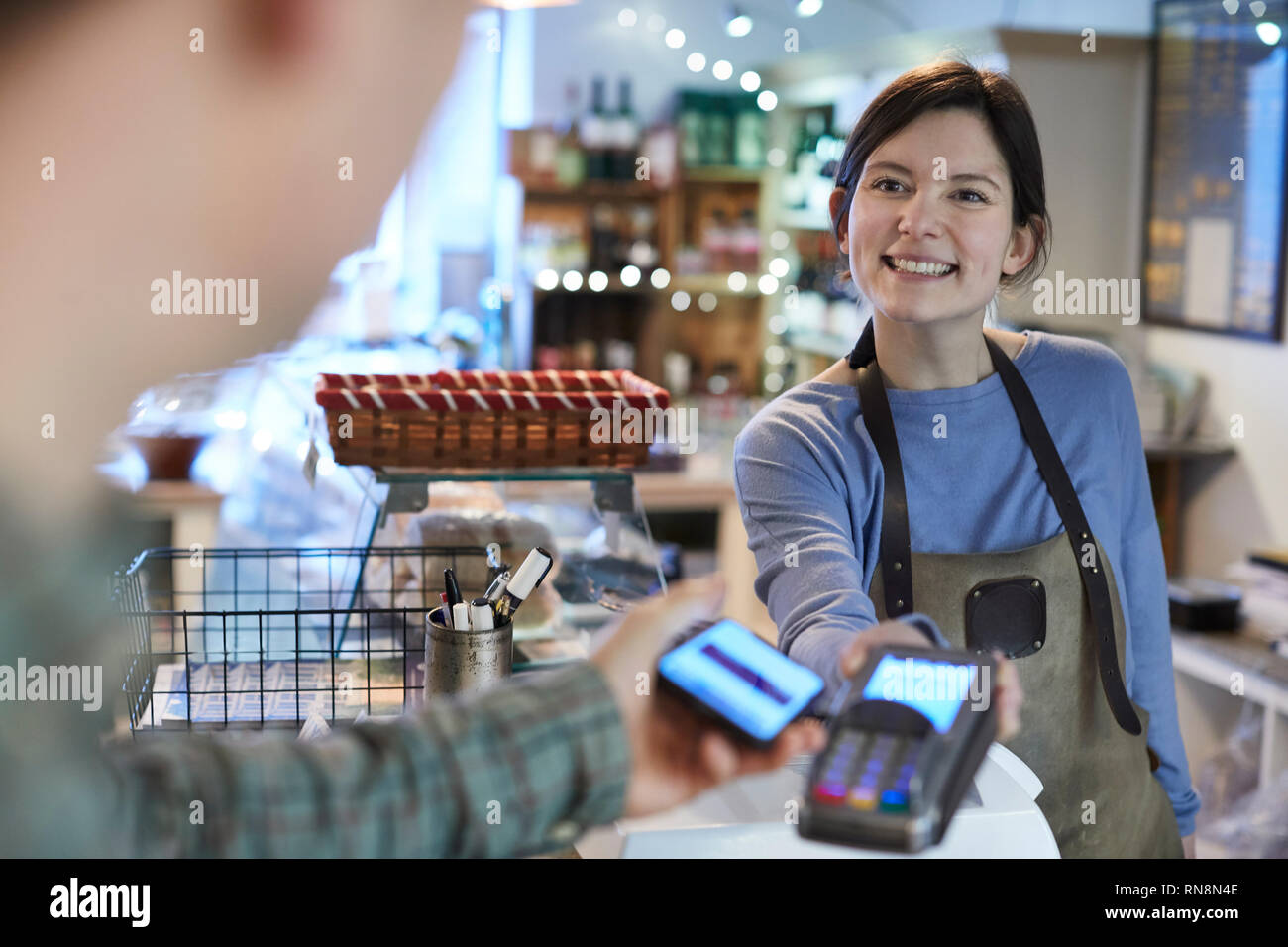 Männliche Kunden kontaktloses Bezahlen für das Einkaufen über Handy in Feinkost Stockfoto
