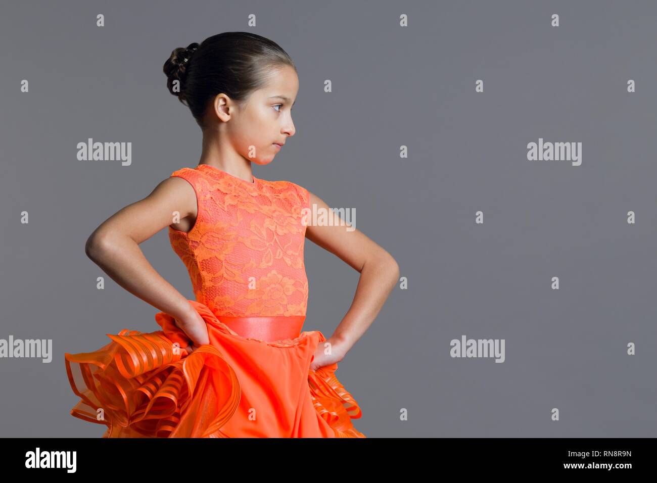 Porträt eines Mädchens, das Kind 9-10 Jahre Tänzer. Sport Gesellschaftstänze, Latino. Mädchen in einem orangefarbenen Kleid auf einem grauen Studiohintergrund, kopieren Raum Stockfoto