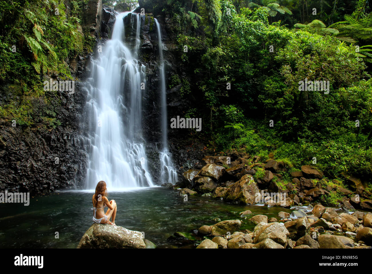 Junge Frau im Bikini sitzen von mittleren Tavoro-Wasserfällen im Bouma National Heritage Park auf Taveuni Island, Fidschi. Taveuni ist die drittgrößte Insel Stockfoto