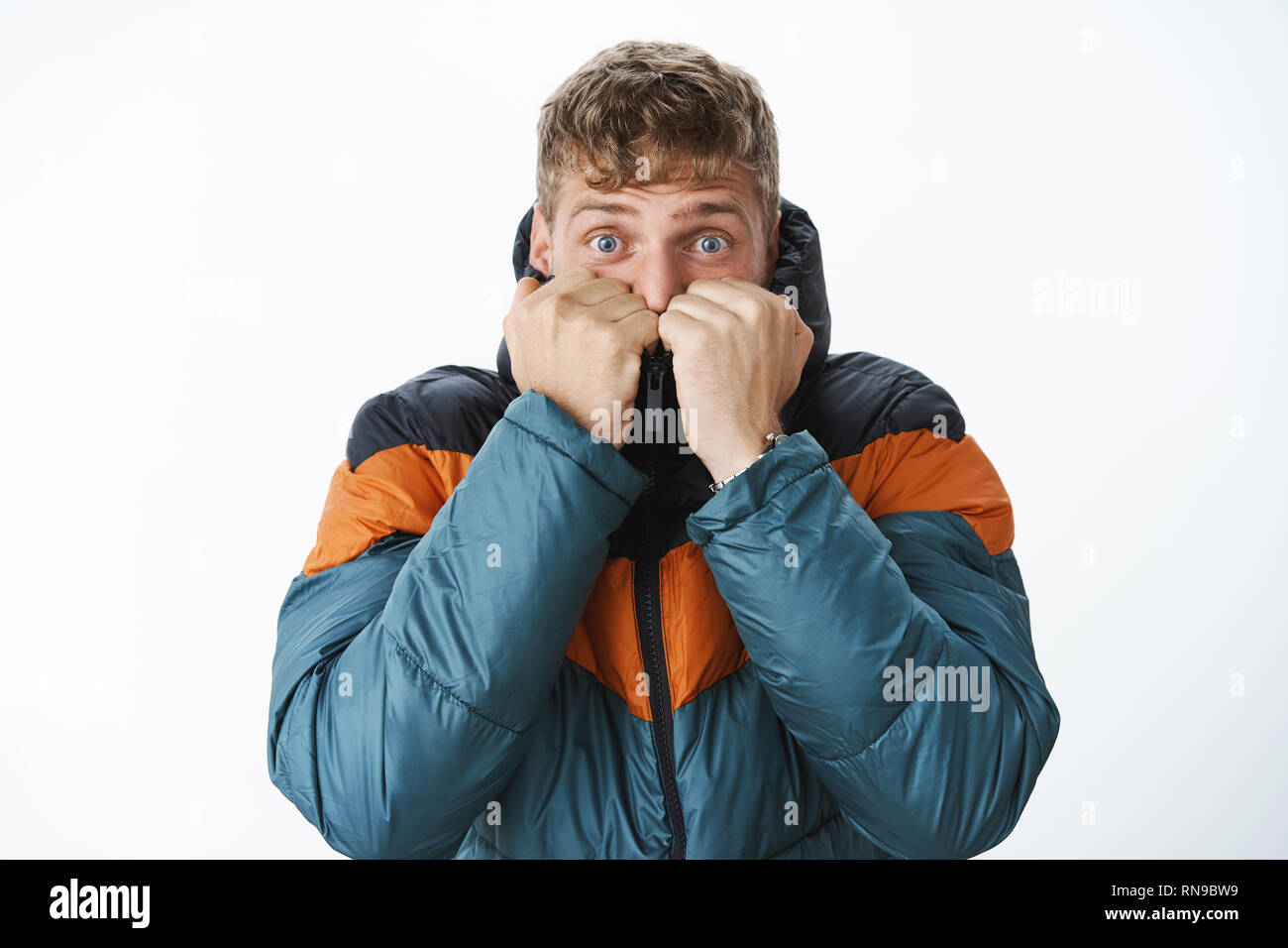 Bereit für den Winter. Gute Angst europäische blonder Mann mit blauen Augen warm ziehen die Schaltmuffe der Puffer Jacke auf dem Gesicht des Ausatmens Luft, stehend Stockfoto