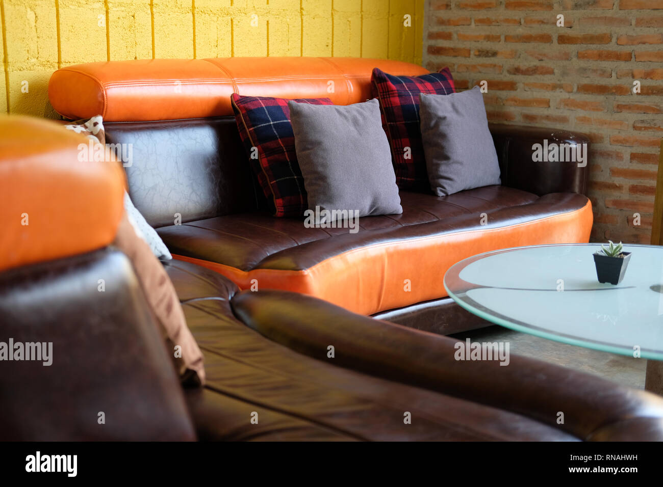 Blue Kissen auf Braun orange leder Sofa Couch neben gelbe Wand Stockfoto