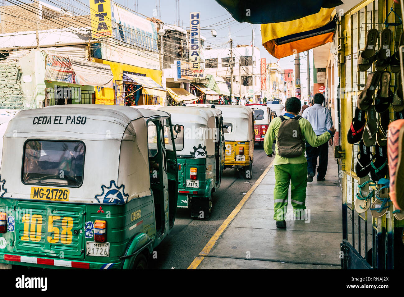 Menschen zu Fuß auf den seitlich durch eine Linie von tuktuk Motorrad Taxis in Ica, Peru. Stockfoto