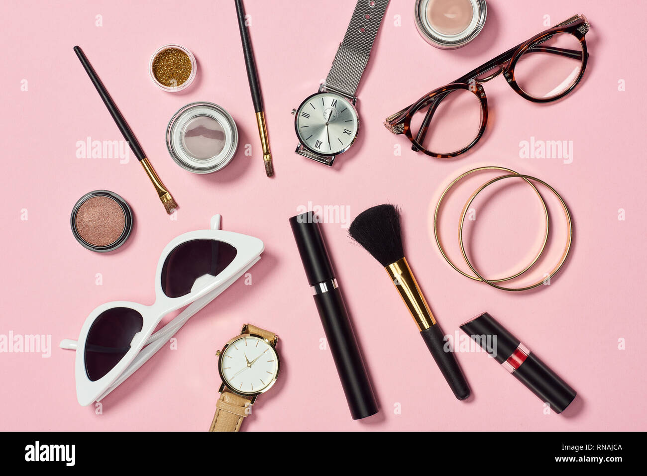 Blick von oben auf die Uhren, Lippenstift, Brillen, Sonnenbrillen, Lidschatten, Rouge, Kosmetikpinsel, Armbänder und Mascara Stockfoto