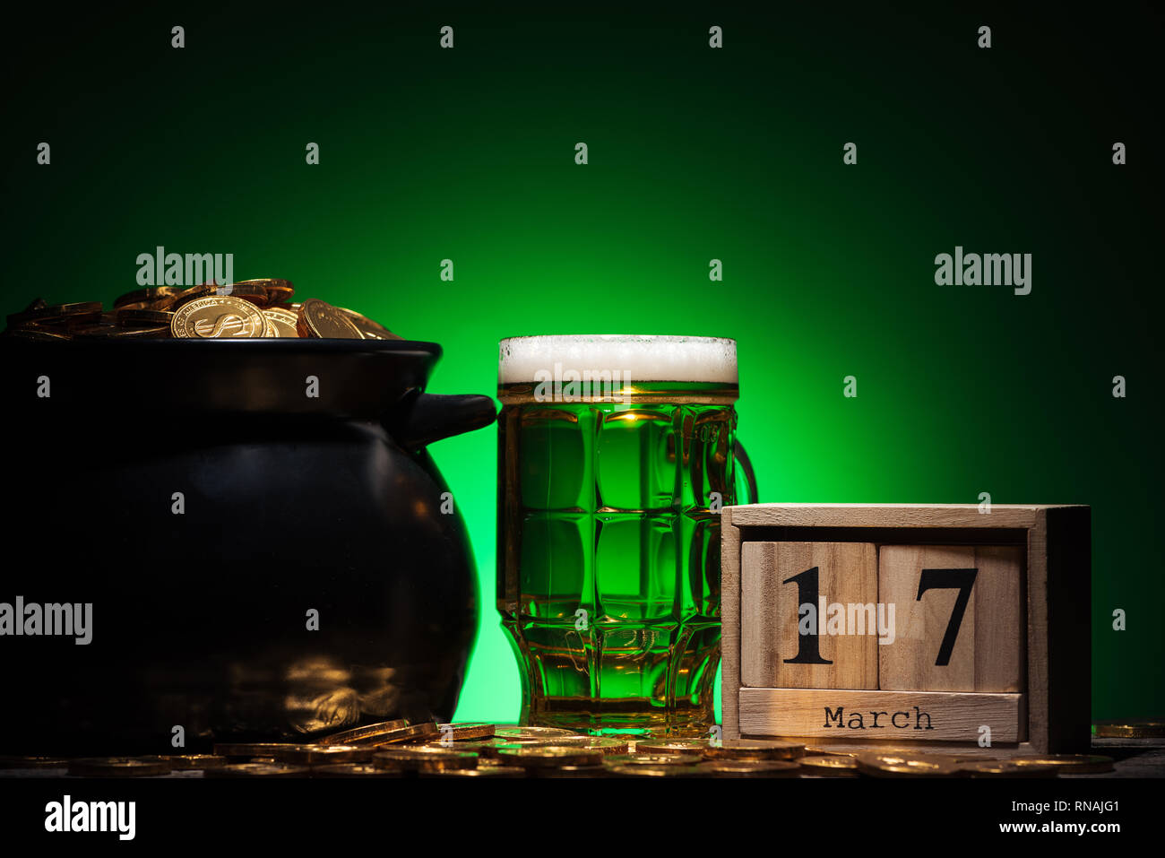Glas irisches Bier in der Nähe von Golden Coins in Topf und Cube Kalender auf grünem Hintergrund Stockfoto