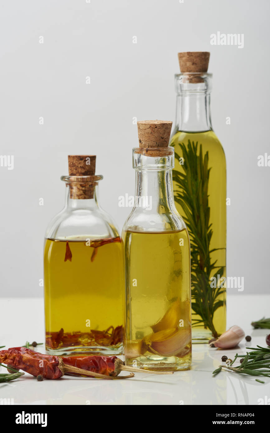 Flaschen Öl aromatisiert mit Rosmarin und verschiedenen Gewürzen auf weiße Oberfläche Stockfoto