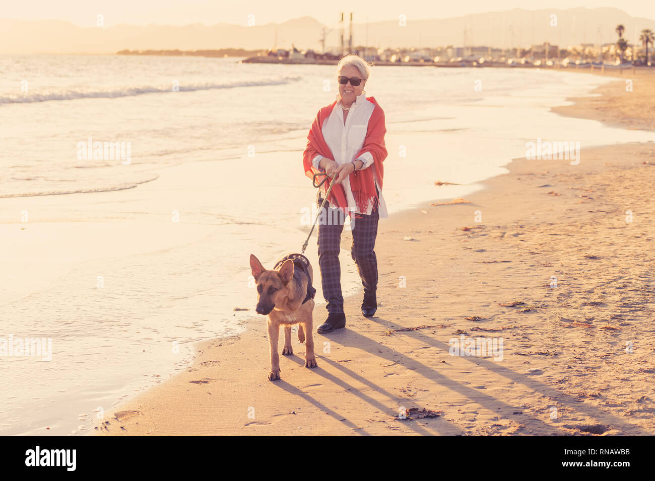 Schönen Ruhestand ältere Frau und pet-deutscher schäferhund Hund wandern entlang der Küste Meer Ozean am Strand in Begleitung Nutzen der Tiere aktiv halten Stockfoto