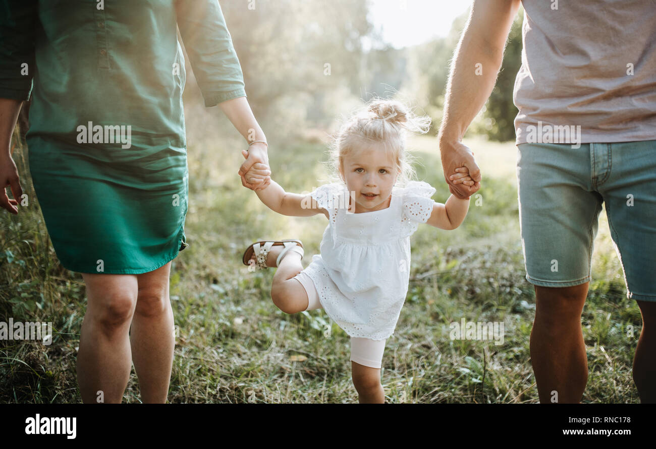 Ein Mittelteil der jungen Familie mit einem kleinen Tochter wandern im sonnigen Sommer Natur. Stockfoto