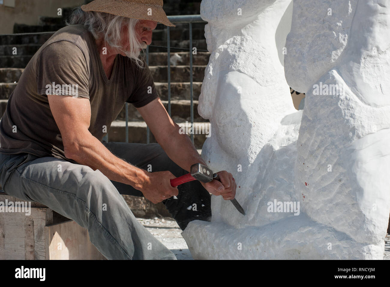 Senior Bildhauer arbeiten im Freien an der Marmorskulptur in seinem Workshop mit Hammer und Meißel Stockfoto