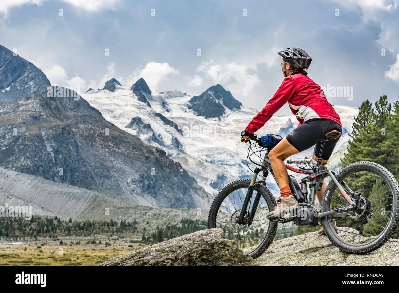 Active Senior, Frau, reiten Ihr e-Mountainbike in das Rosegtal unterhalb der Gletscher und Gipfel der Sella Gruppe und Piz Roseg Stockfoto