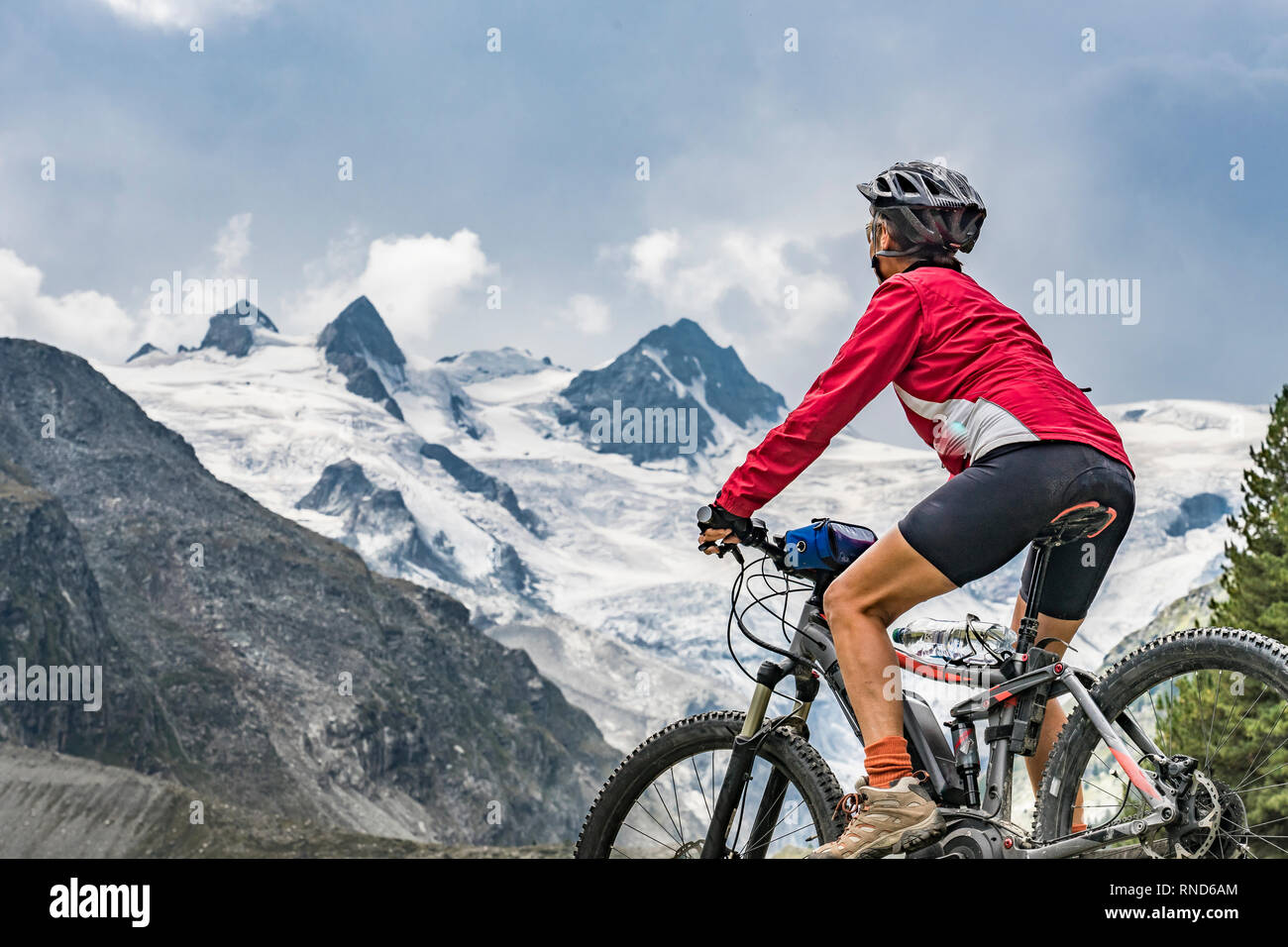 Active Senior, Frau, reiten Ihr e-Mountainbike in das Rosegtal unterhalb der Gletscher und Gipfel der Sella Gruppe und Piz Roseg Stockfoto