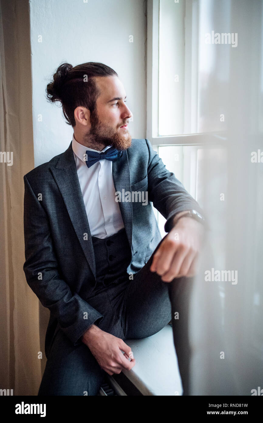 Ein schöner Hipster junger Mann mit Anzug saß auf dem Fensterbrett auf einer überdachten Partei. Stockfoto