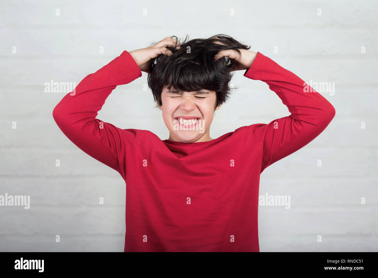Junge sein Haar für Kopfläuse gegen Ziegel Hintergrund verkratzen Stockfoto