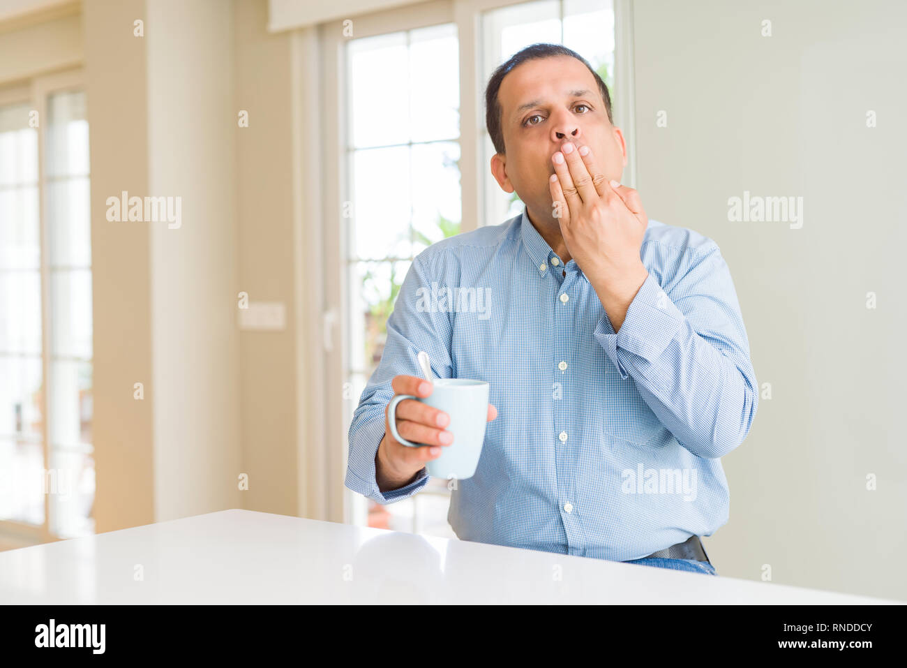 Mittleres Alter Mann trinkt Kaffee am Morgen zu Hause decken den Mund mit der Hand mit Schande für den Fehler, den Ausdruck von Angst erschüttert, die in der Stille Angst, Sek Stockfoto