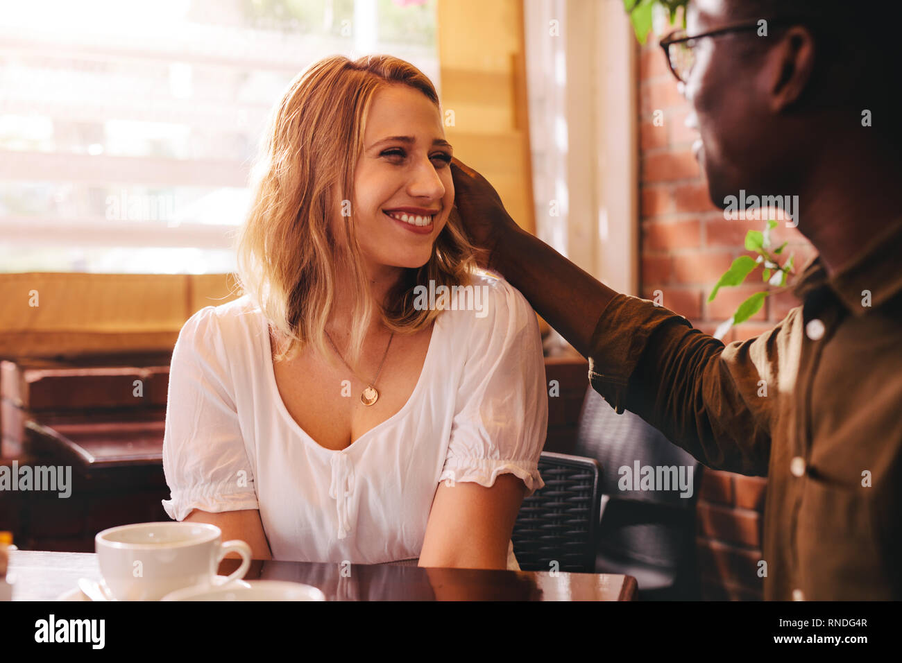 Interracial Paare. im Café sitzen. Lächelnde Frau mit ihrem fürsorglichen Freund im Cafe. Stockfoto