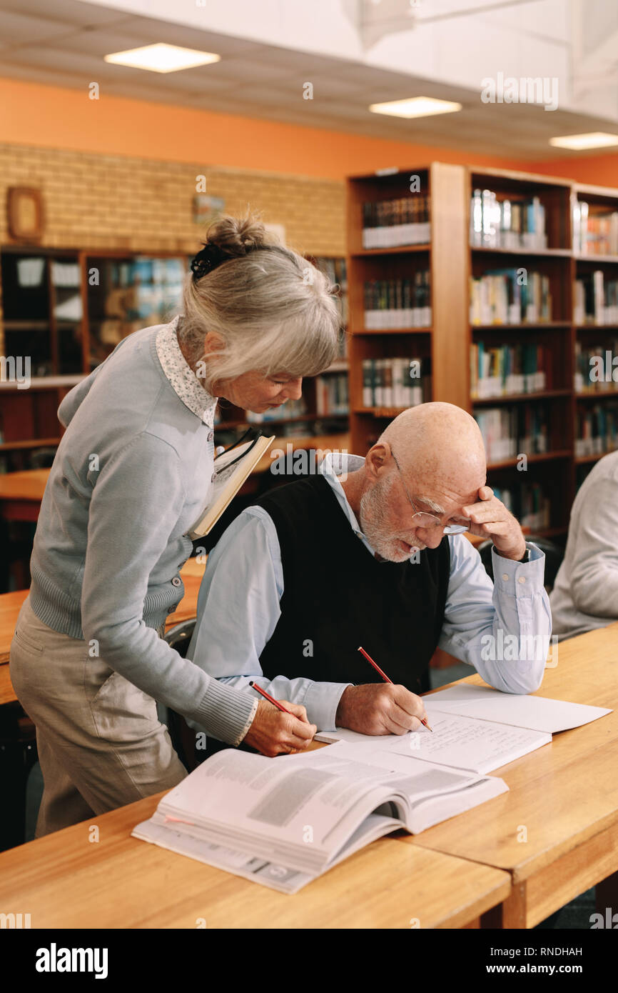 Frau Professor Überprüfung der Arbeit eines älteren Schüler im Klassenzimmer. Ältere Menschen Schreiben von Notizen in seinem Buch, während ein älterer Lektor ihn leitet. Stockfoto