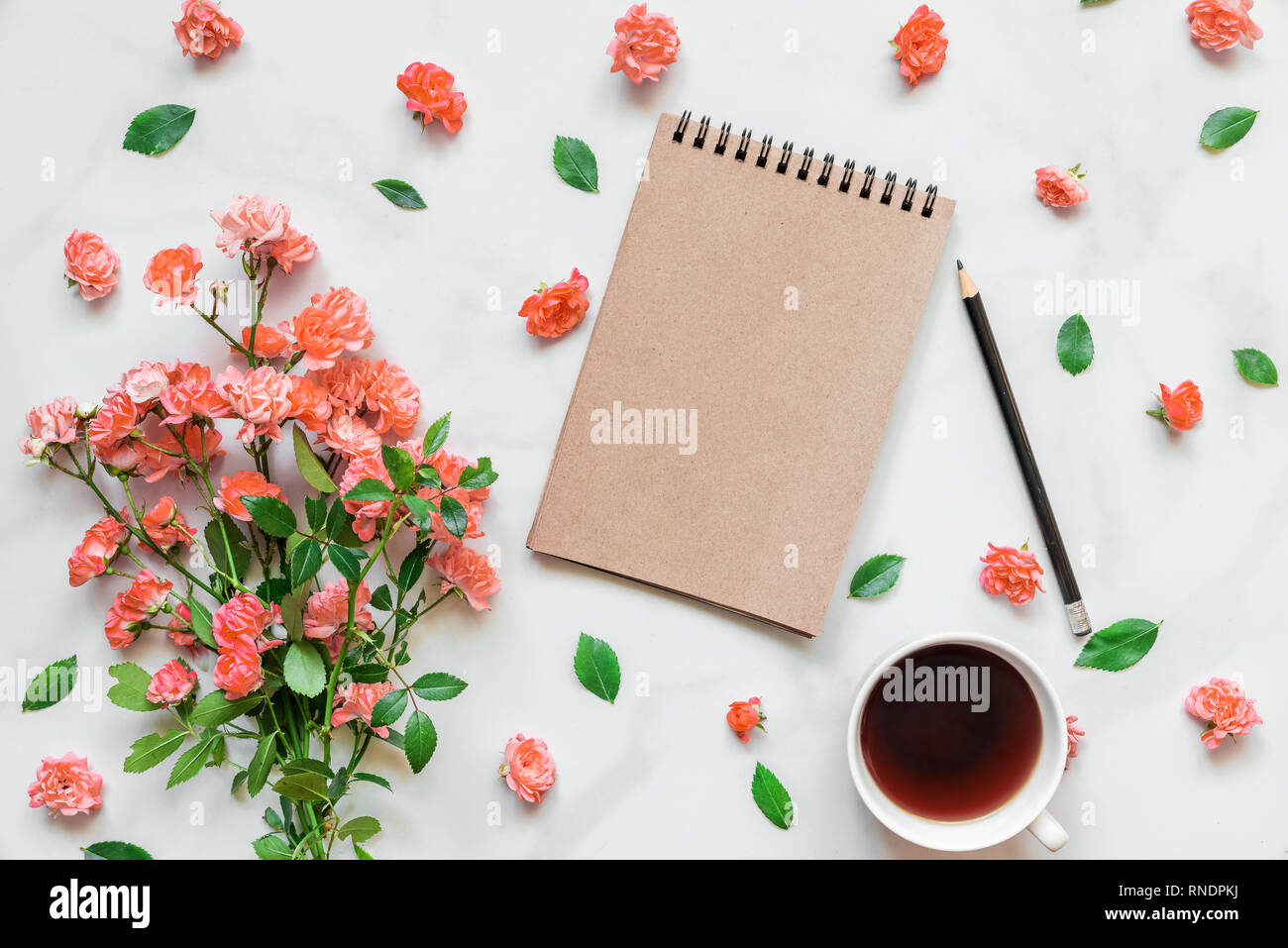 Leere notepad mit Blumenstrauß aus Rosen in lebende Koralle Farbe und Kaffee Tasse im Rahmen der Knospen auf weißem Marmor tisch. Hochzeit Hintergrund. Flach Stockfoto