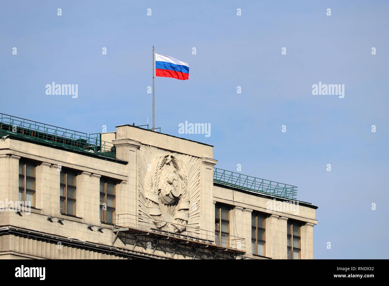 Russische Flagge auf dem Parlamentsgebäude in Moskau gegen den blauen Himmel. Fassade der Staatsduma Russlands mit sowjetischen Wappen Stockfoto