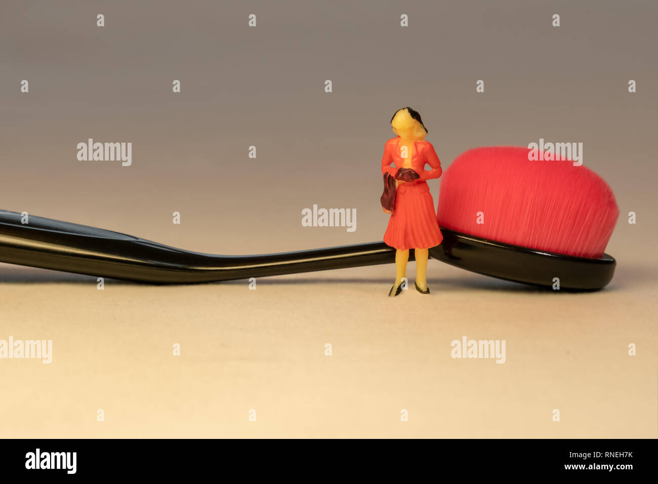 Miniatur Frau in orange Kleid neben Schwarz oval Make-up-Pinsel. Schönheit und Hautpflege. Stockfoto