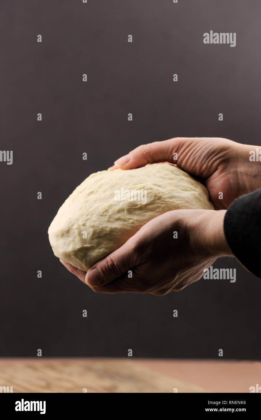 Jemand eine Pizza Teig mit beiden Händen auf einem dunklen Hintergrund Stockfoto