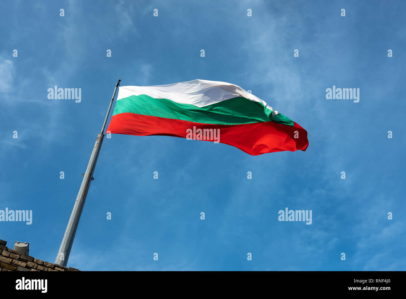 Bulgarische Flagge von Fahnenmast wird schräg gegen den blauen Himmel mit Spuren von Licht, weiß cirrus Cloud gerahmt Stockfoto