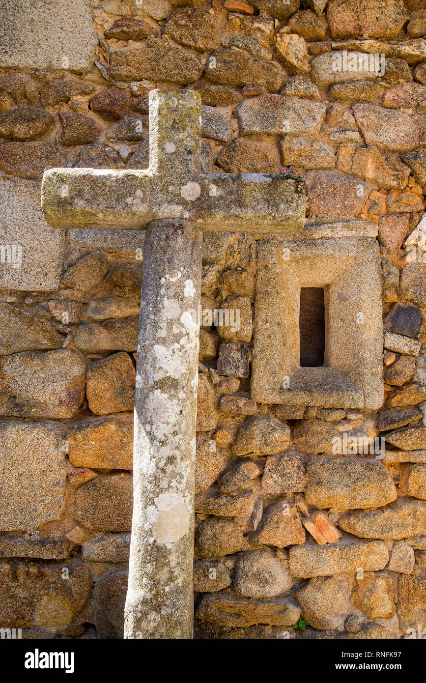 Steinernes Kreuz gegen die Mauer aus Stein. San Martin del Castañar, Sierra de Francia Nature Reserve, Provinz Salamanca, Castilla Leon, Spanien. Stockfoto