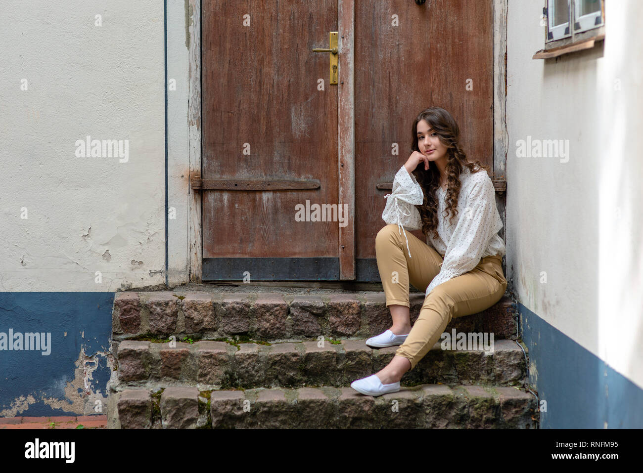 Eine junge, hübsche, dunkelhaarige Frau sitzt auf einem alten Haus Treppen. Kopieren Sie Platz. Stockfoto