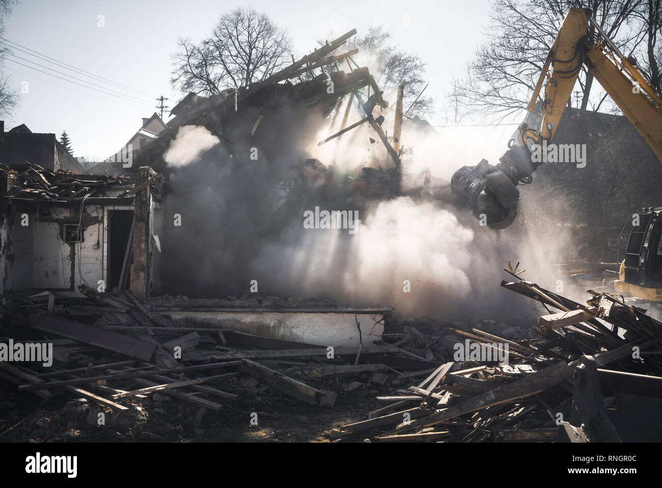 Abriss eines alten Deutschen Haus mit einem Bagger. Haus stürzt in eine Staubwolke und Sonnenstrahlen. Baustelle. Stockfoto