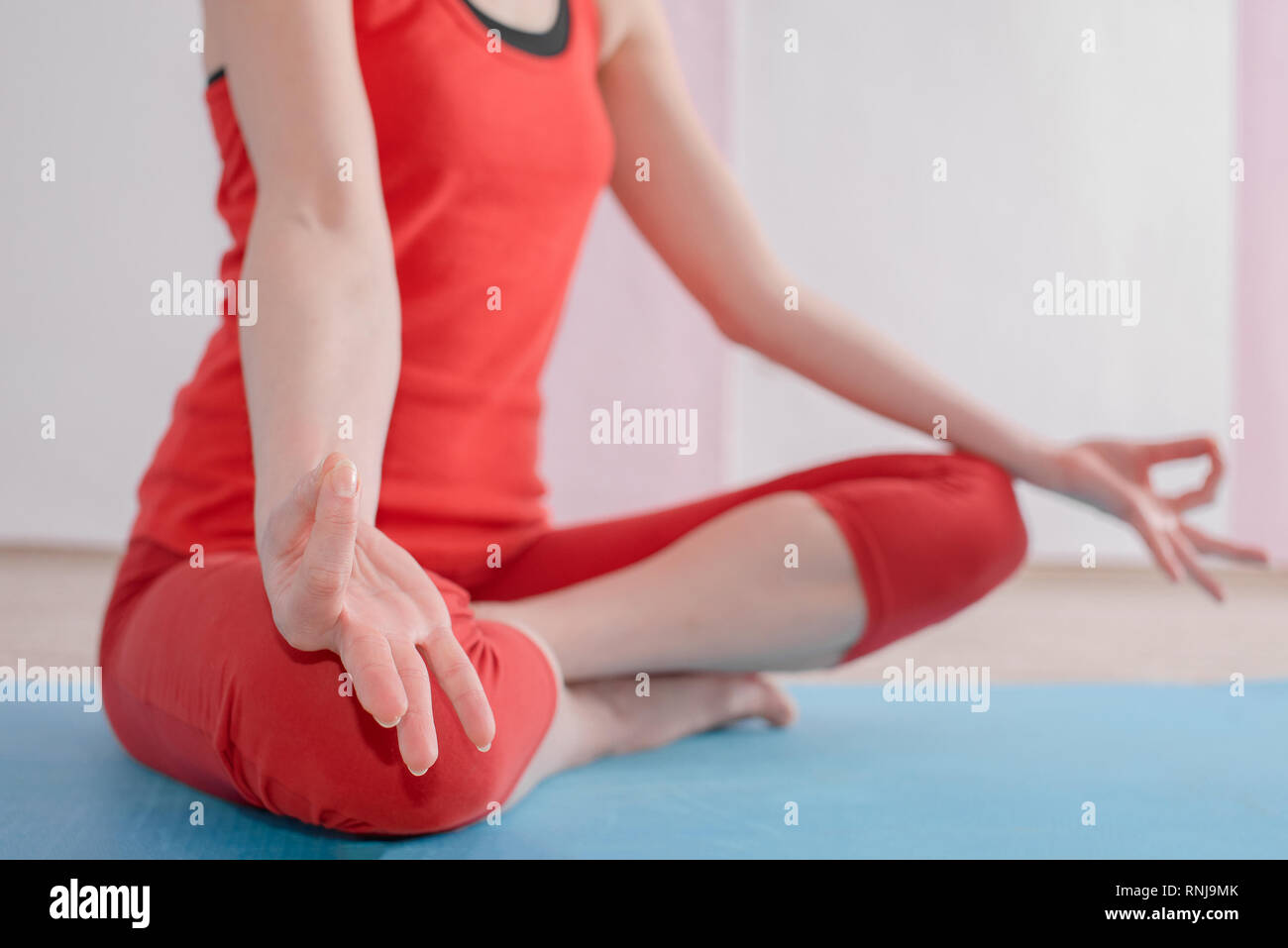 Ein Mädchen in einem roten Sport einheitliche sitzt in einem Lotus Position während des Yoga in der Halle. Das Mädchen macht mudras Hände. Stockfoto