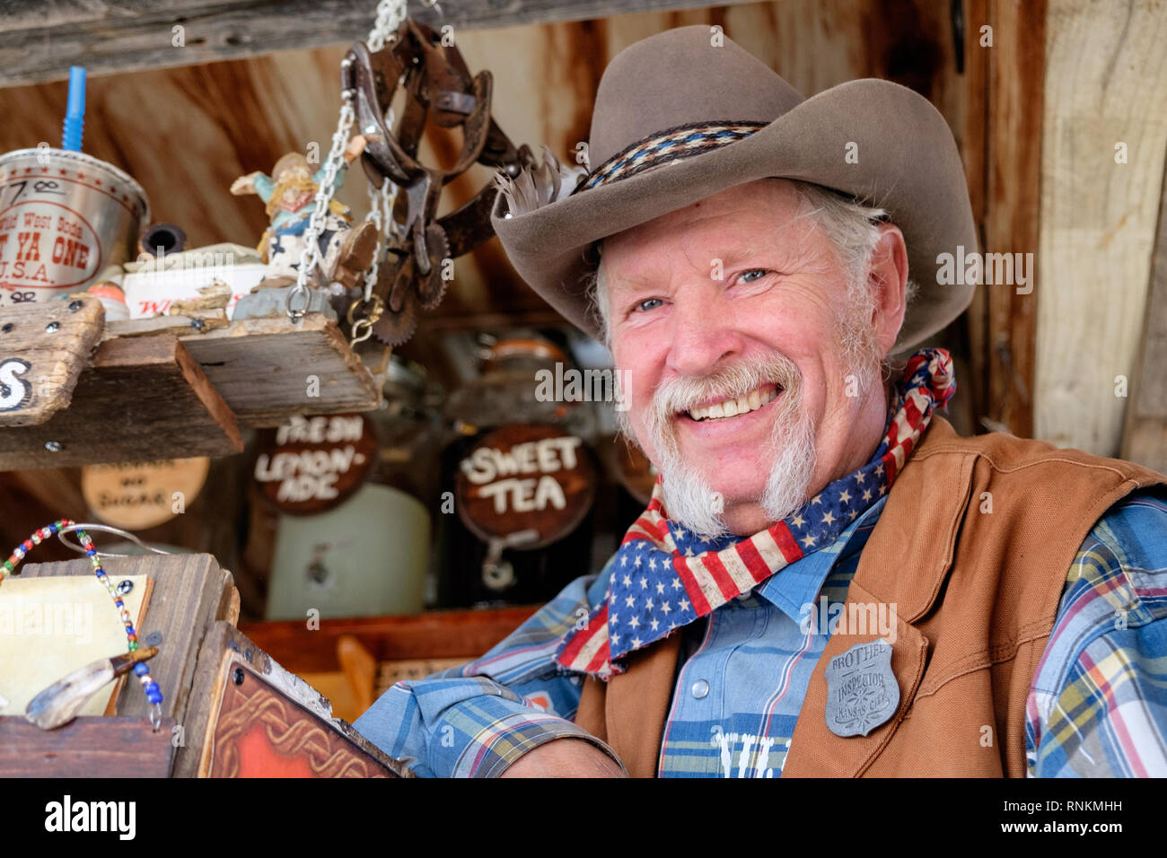 Staycation. Lächelnder texanischer Cowboy mit Cowboyhut, Schal und weißem Hufeisenbart am Wild West Soda Marktstand. Trade Days Market. Stockfoto