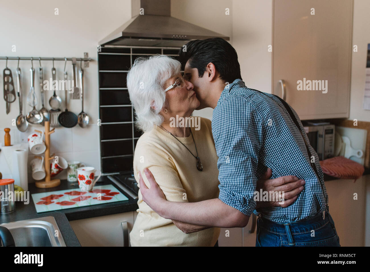 Teenage Boy ist ein Lächeln für die Kamera, während seine Großmutter seine Wange küsst. Stockfoto