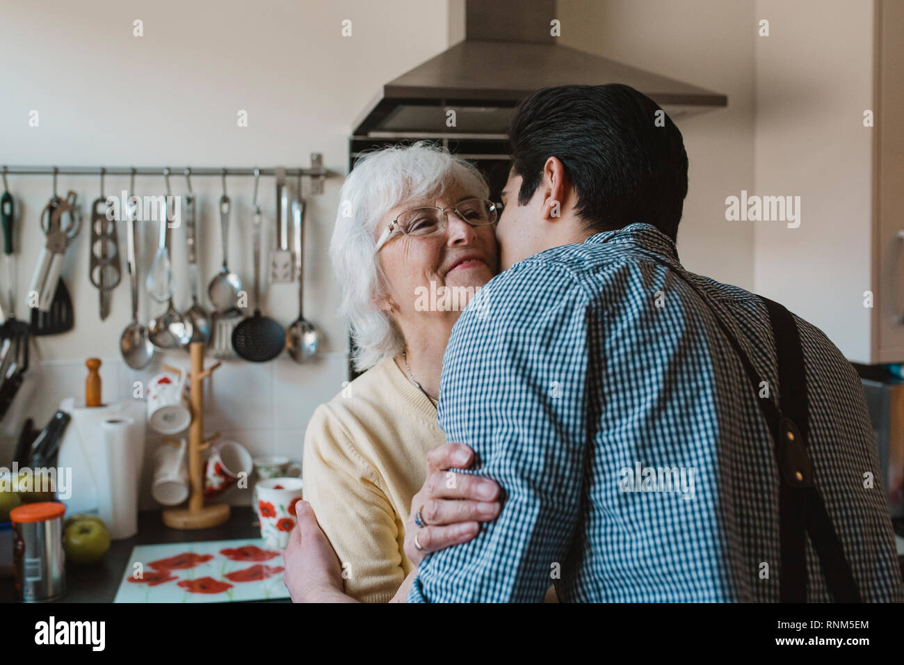 Teenage Boy ist ein Lächeln für die Kamera, während seine Großmutter seine Wange küsst. Stockfoto