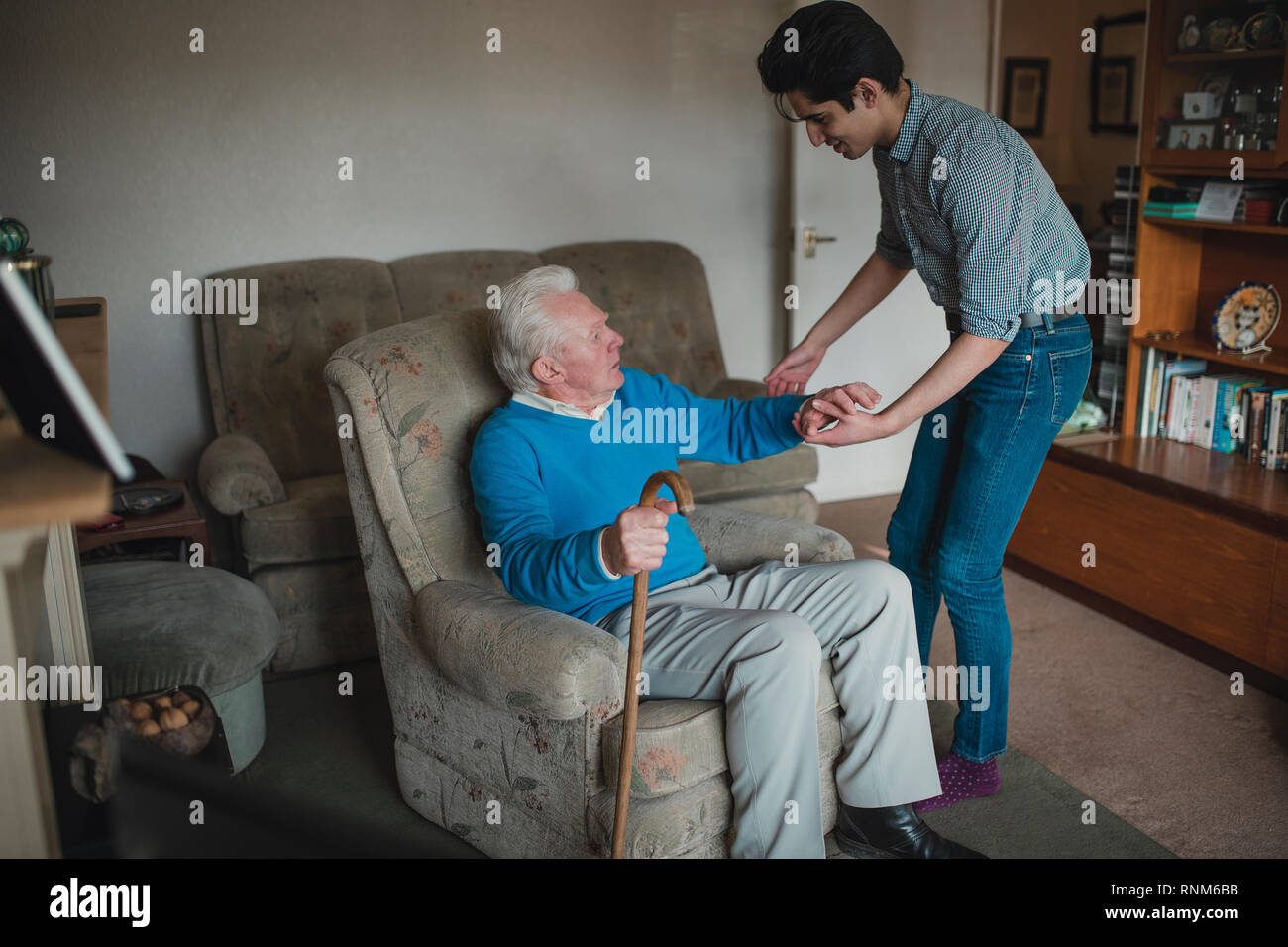 Teenager Jungen hilft, sein Großvater aus seinem Sessel. Stockfoto