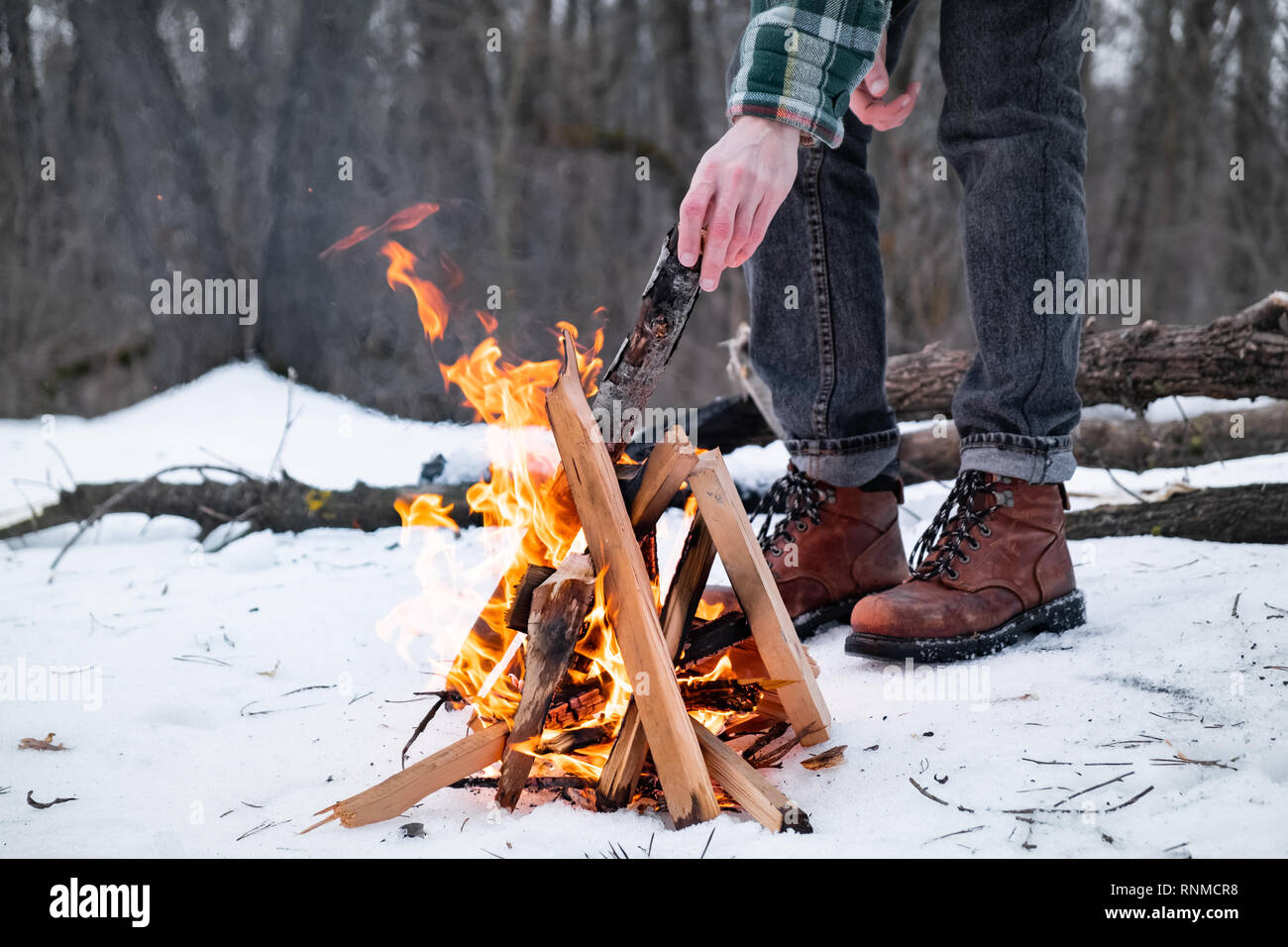 Ein Lagerfeuer in einem verschneiten Wald. Männliche Person in der Nähe eines Feuers an einem Wintertag im Wald Stockfoto