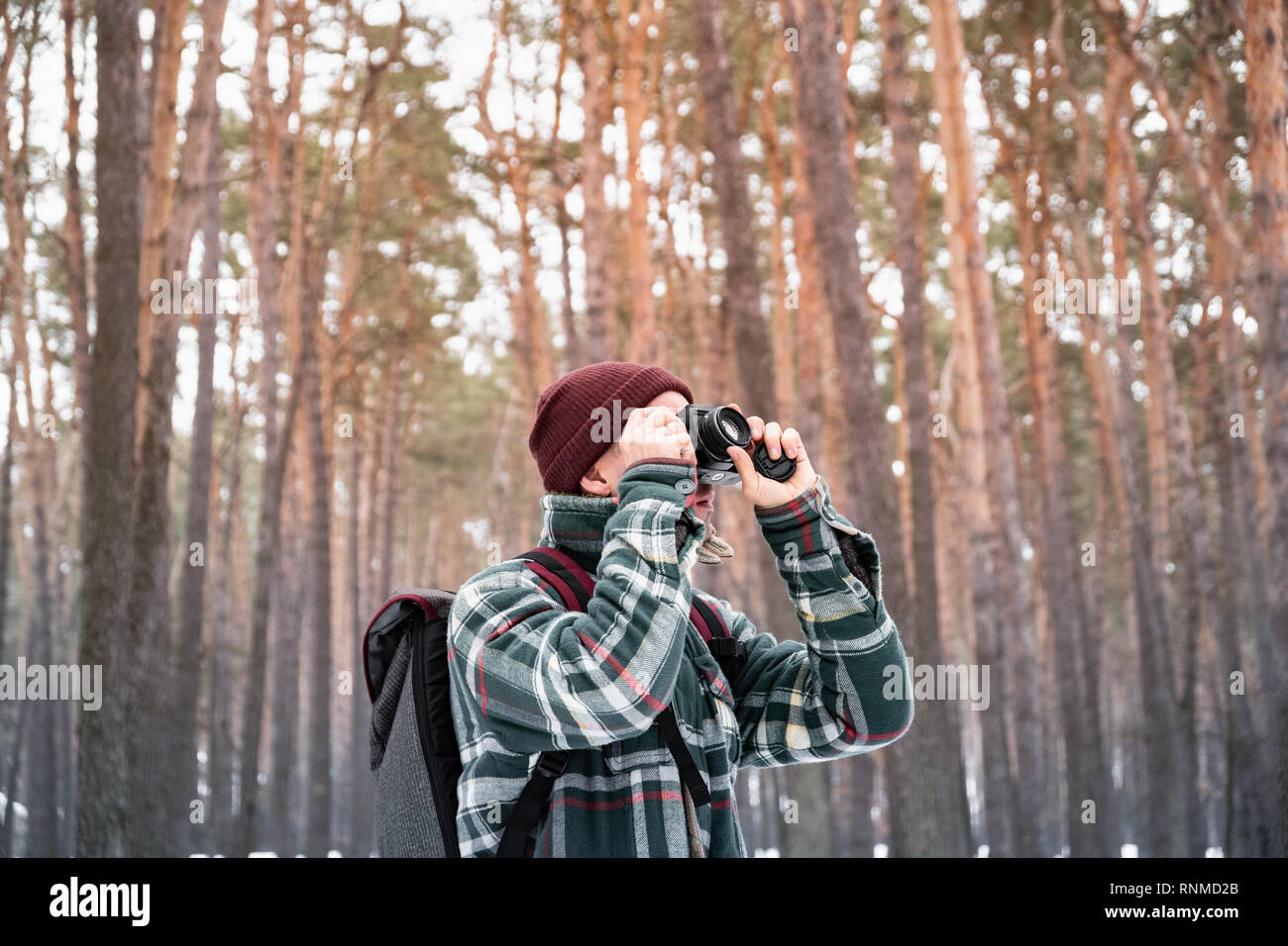 Wandern männliche Person im Winter Wald Foto nehmen. Mann in karierten winter Shirt im schönen schneebedeckten Wäldern verwendet alte Filmkamera Stockfoto