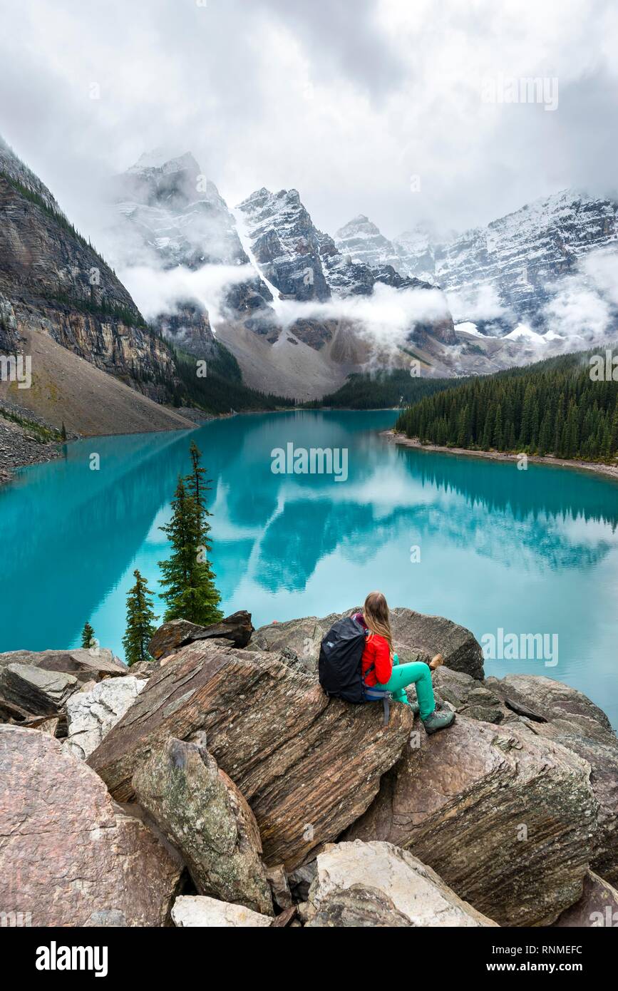Junge Frau vor einem See in Bergwelt suchen sitzen, Wolken zwischen Bergspitzen, Reflexion in der türkisfarbenen See, Moräne L Stockfoto