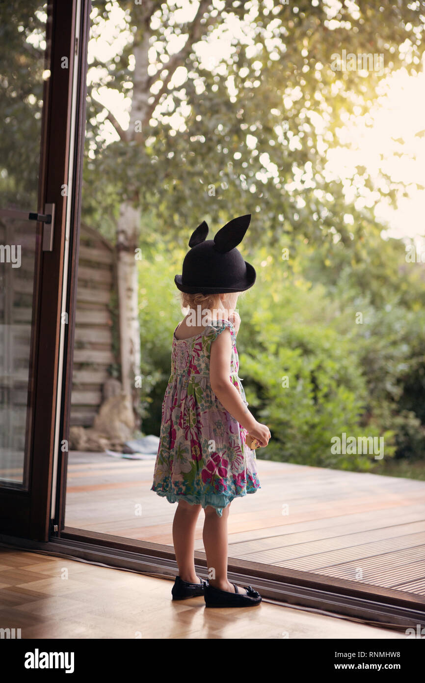 Kleines Mädchen mit Hase hat, zögernd stand neben einer offenen Terrasse Tür Stockfoto
